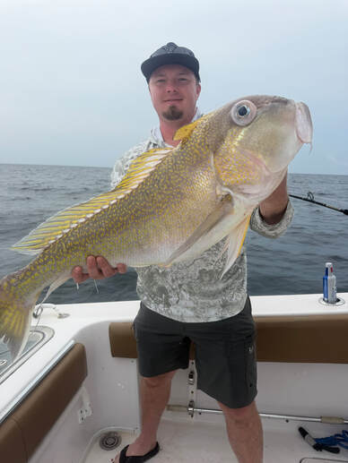 An angler aboard a boat holding a golden tilefish with a large eye and gold markings